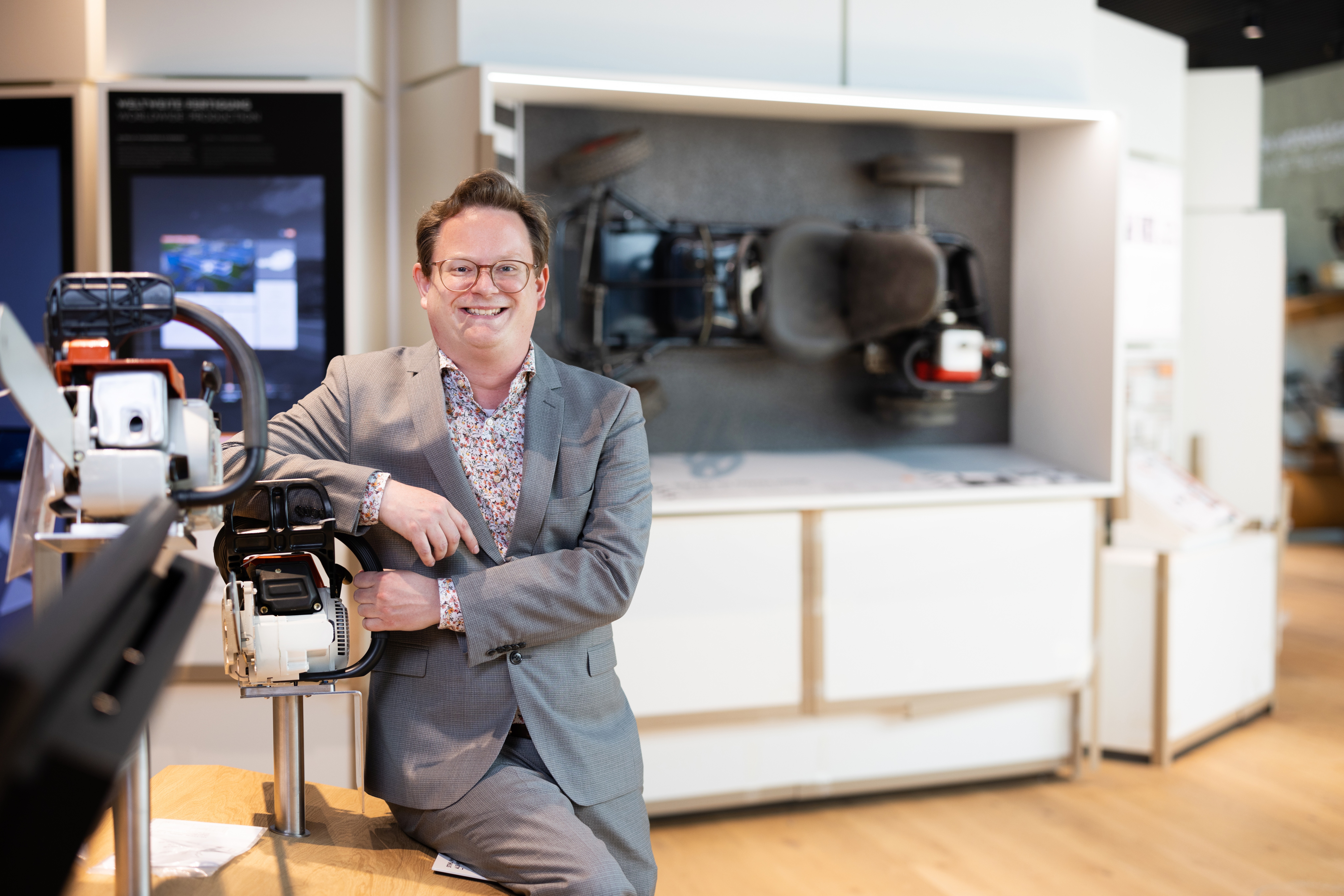 STIHL Unternehmensarchivar Dr. Michael Hartmann in der Markenwelt auf einem Tisch neben Motorsägen sitzend